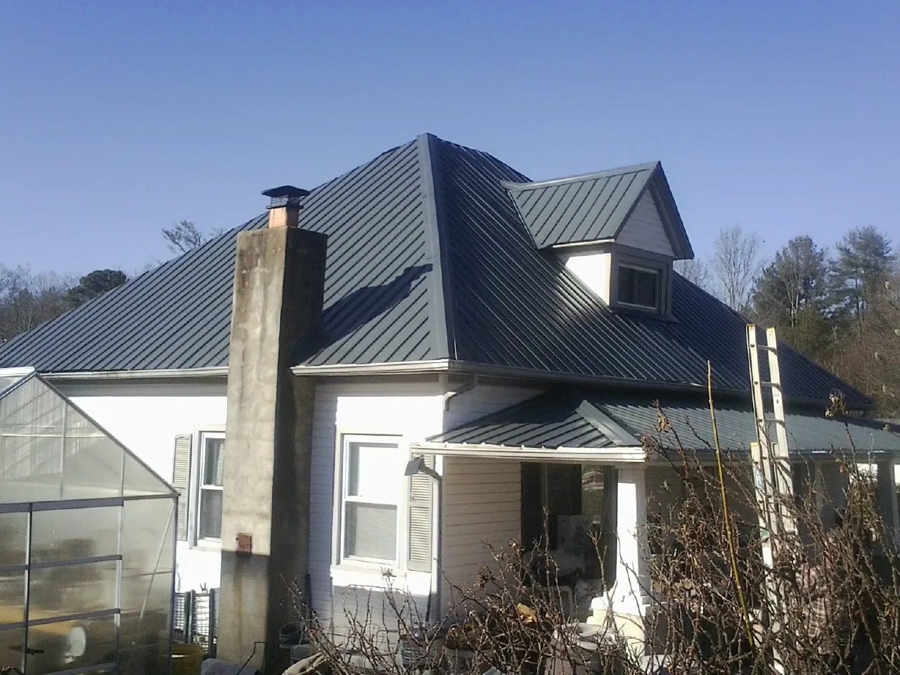 Dark blue standing seam metal roof on a white farmhouse with dormer — Slate & Tile Roof Repair by Roofing Brothers in Chariton