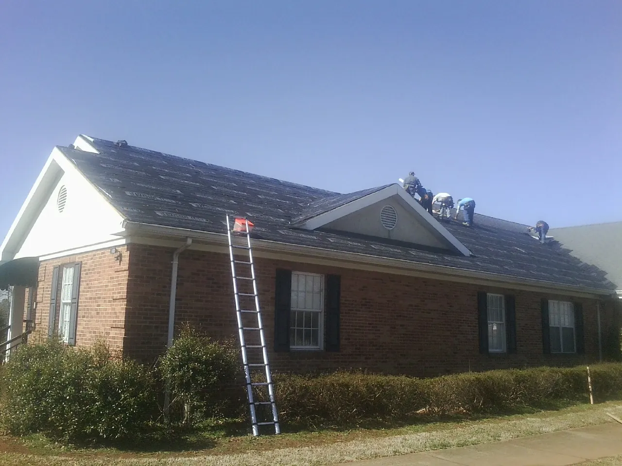 Crew tearing shingles off a brick ranch roof with a ladder set — Emergency Roof Repair work by our crew in Chariton