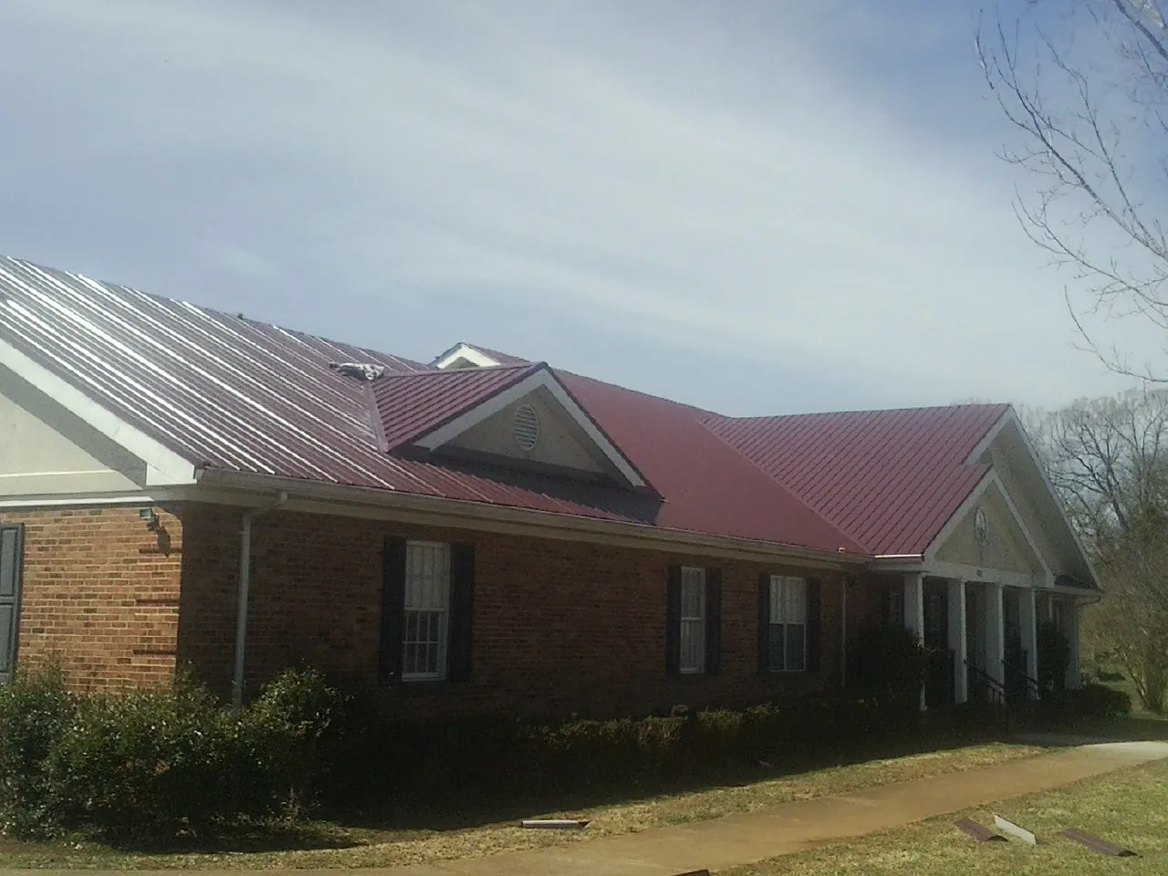 Red metal roof with gabled entries on a long brick building, from a Hail Damage Roof Repair job in Chariton