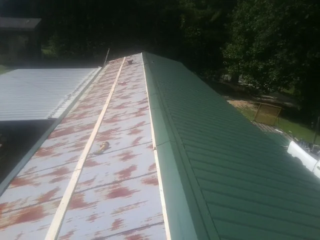 Old rusted panels beside newly installed green metal roofing — Wind Damage Roof Repair by Roofing Brothers in Chariton