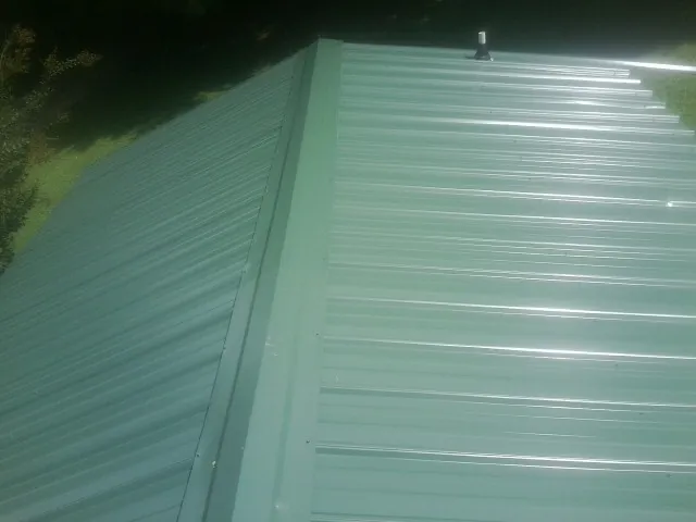 New green metal panels meeting at the ridge of a roof — Flat Roof Repair work by our crew in Chariton
