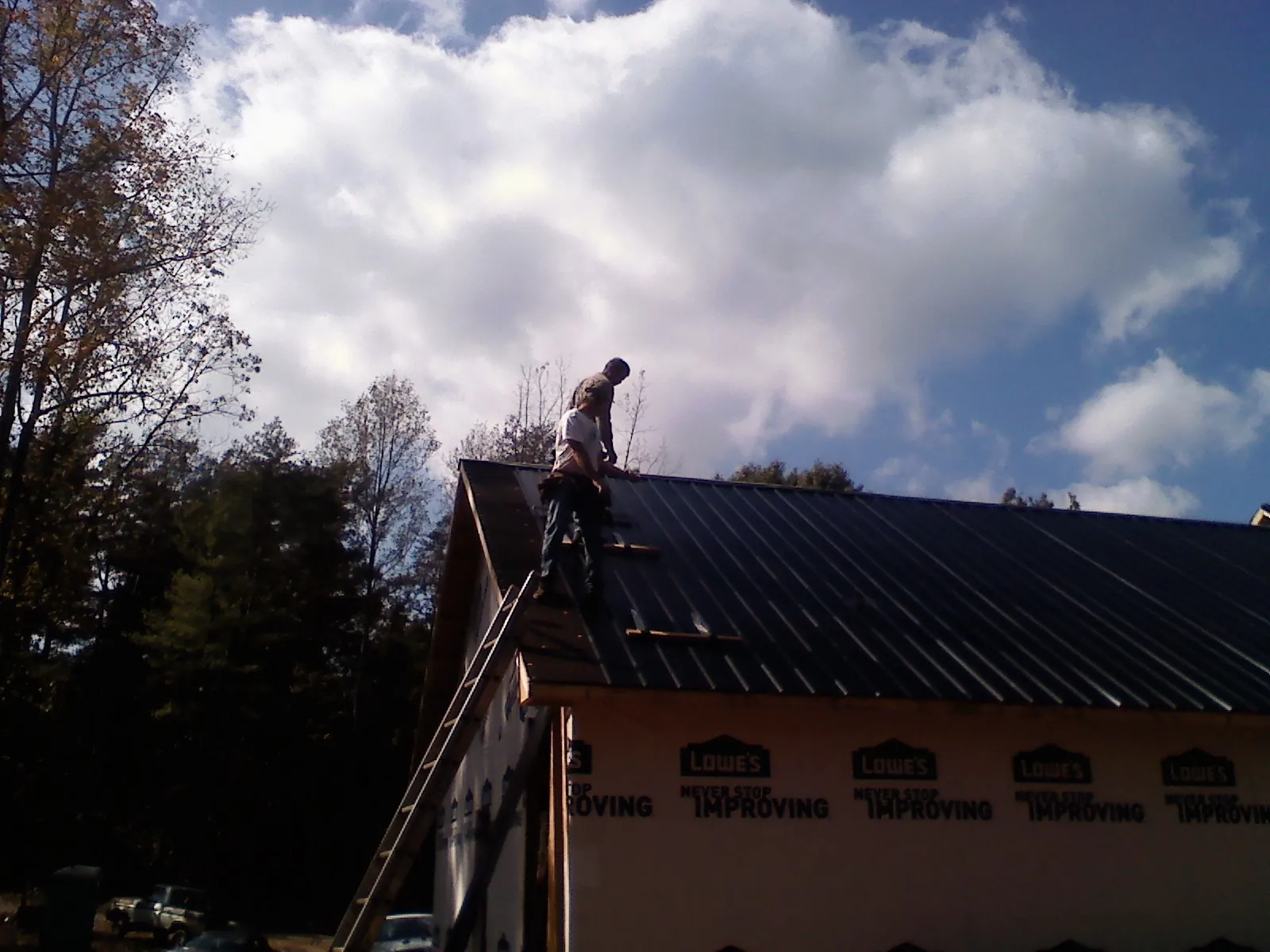 Roofer fastening dark metal panels high against a cloudy sky, from a Roof Inspection job in Chariton