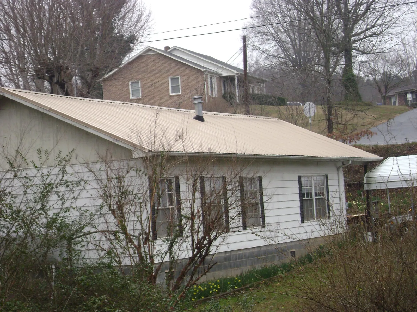 Tan metal roof on a white sided house set into a hillside — Commercial Roofing by Roofing Brothers in Chariton