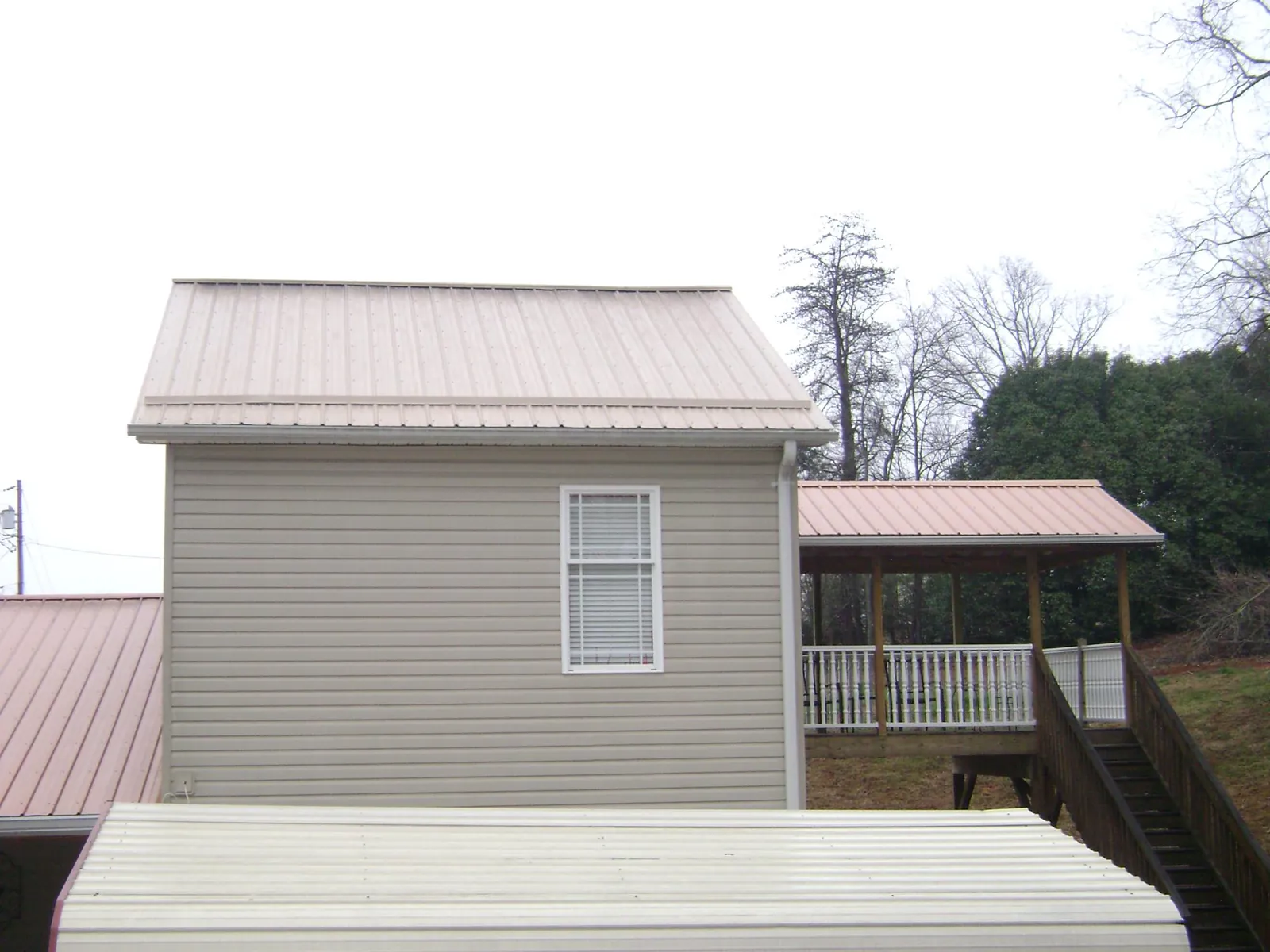 Tan metal roofs on a two story addition and attached porch, from a Roof Replacement job in Chariton