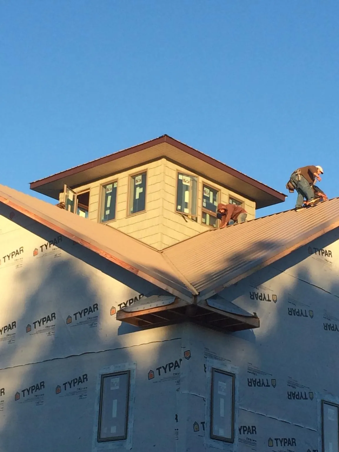 Roofers working around a rooftop cupola on a new metal roof at sunset — Roof Waterproofing in Chariton by Roofing Brothers